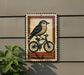 a decorative sign with a bird riding a bicycle, mounted on a wall.