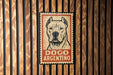 A sign featuring a dog's face with the text "DOGO ARGENTINO" on it, mounted on a wooden wall.