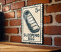 A metal sign with a sleeping bag illustration on it, mounted on a brick wall.