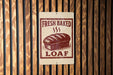 A sign that reads "FRESH BAKED LOAF" is displayed on a wooden wall.