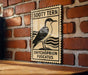 a wooden sign with a black and white illustration of a bird, mounted on a brick wall.