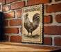 A vintage-style metal sign with a rooster illustration is mounted on a brick wall.