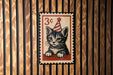 A vintage-style 3-cent stamp featuring a cat wearing a party hat, displayed on a wooden background.