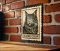A metal sign featuring a black and white illustration of a Maine Coon cat, mounted on a brick wall.
