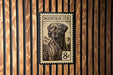 A metal plate with a printed image of a dog, resembling a postage stamp, mounted on a wooden wall.