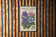 A postage stamp featuring a floral illustration of purple and pink flowers, with the text "African Violet Collection" and the number "29" printed on it.