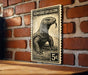 A black and white illustration of a Komodo dragon on a postage stamp-like frame is displayed on a wooden surface against a brick wall.