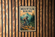 A vintage-style metal sign with a mountain landscape and a person riding a bicycle, mounted on a wooden wall.