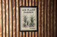 a sign that reads "Air Plant Garden Forever" with a black and white illustration of a plant on it, mounted on a wooden wall.