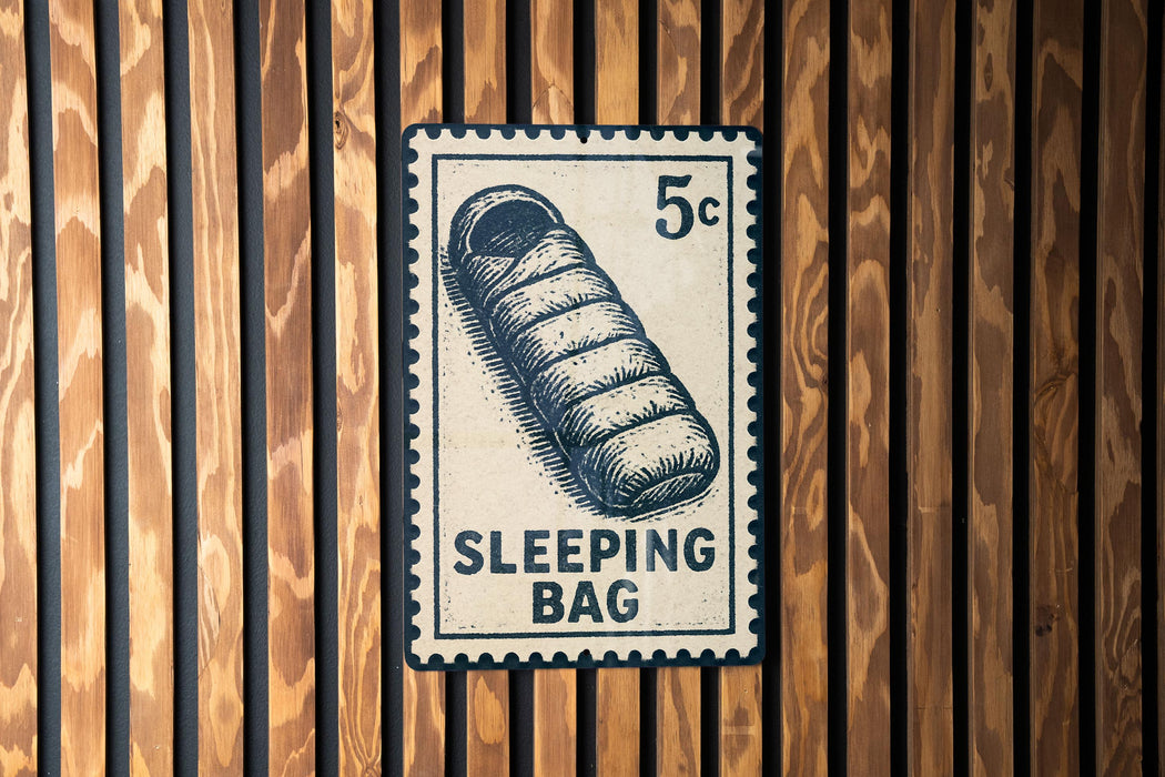A sleeping bag postage stamp is displayed on a wooden wall.