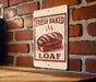 A sign on a brick wall that reads "FRESH BAKED LOAF", featuring an illustration of a loaf of bread.