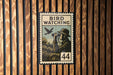A vintage-style stamp depicting a man using binoculars to observe a bird, with the text "BIRD WATCHING" and the number "44" printed on it.