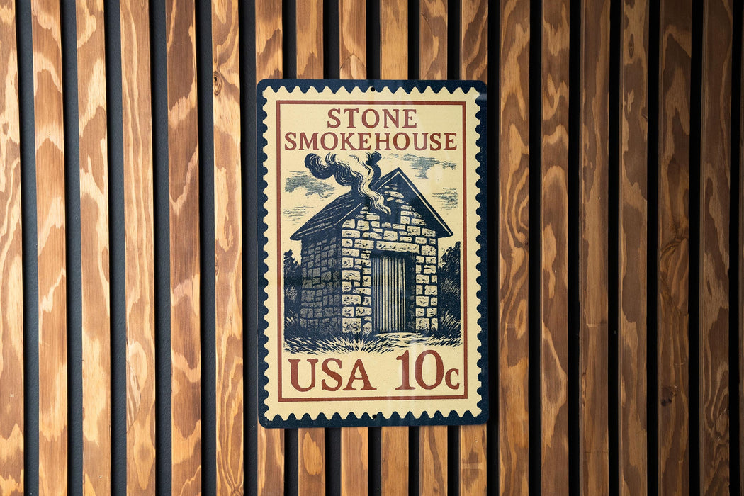 A vintage-style stamp or postcard with the text "STONE SMOKEHOUSE" and "USA 10c" printed on it, mounted on a wooden wall.