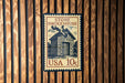A vintage-style stamp or postcard with the text "STONE SMOKEHOUSE" and "USA 10c" printed on it, mounted on a wooden wall.