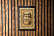 A honey jar is depicted on a wooden wall, with a stamp-like design around it.