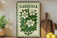 A decorative sign with a floral design, featuring white flowers and green leaves, is displayed on a shelf next to a wooden cutting board and a potted plant.