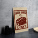 A sign advertising "Fresh Baked Loaf" is displayed on a table, with a stack of black cups and a woven basket nearby.