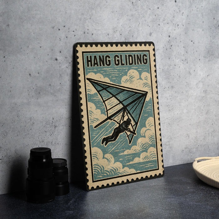A framed poster of a hang glider is displayed on a table, with a stack of black camera lenses and a white plate nearby.
