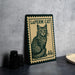 A framed image of a cat, resembling a postage stamp, is displayed on a table next to some black camera lenses.
