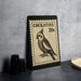A Cockatiel postage stamp is displayed on a table, with a stack of black camera lenses and a woven basket nearby.