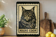A framed image of a Maine Coon cat is displayed on a shelf, accompanied by a wooden cutting board, a potted plant, and some lemons.