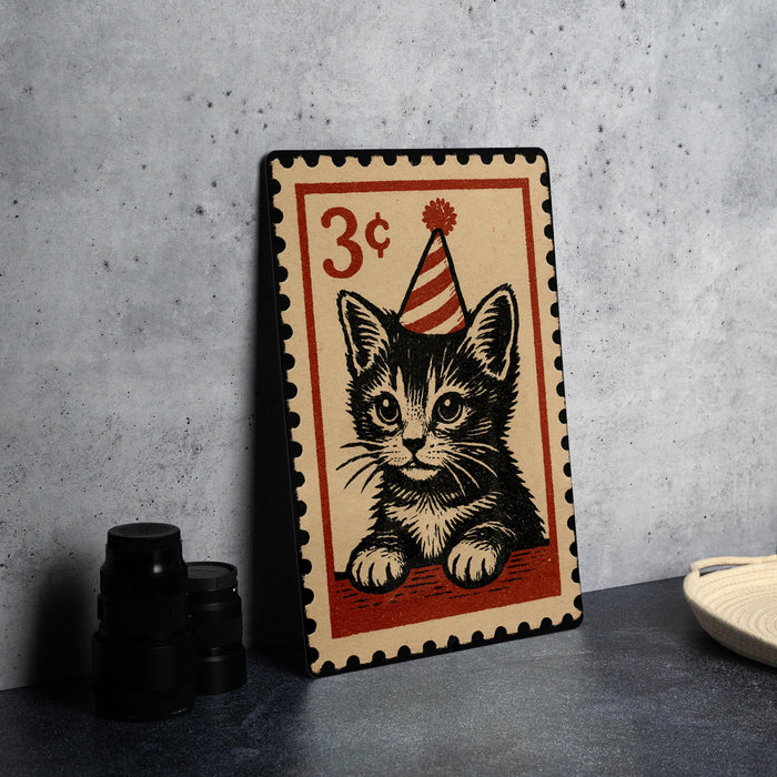 A metal frame with a printed illustration of a cat wearing a party hat, resembling a postage stamp design.
