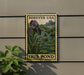 A metal sign with a postage stamp design hangs on a wall, depicting an iris pond surrounded by lily pads.