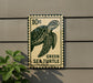 A green sea turtle stamp is attached to a wall, with a plant visible to the left.