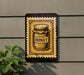 A sign with a jar of honey on it is mounted on a wall, with a plant visible to the left of the sign.