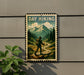 A vintage-style metal sign with a hiker walking on a trail, surrounded by mountains and pine trees, mounted on a wall.