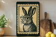 a framed illustration of a rabbit wearing glasses, placed on a shelf next to a wooden cutting board and some lemons.
