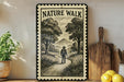 A framed illustration of a person walking on a path through a forest, with mountains in the background, is displayed on a wall next to a wooden cutting board and some potted plants.