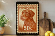 A framed stamp featuring a dog's head, with the text "Pudelpointer" and the number "50c" printed on it. The stamp is placed on a shelf next to a wooden cutting board and some kitchen utensils.