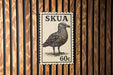 A postage stamp featuring a bird, likely a seagull, is displayed on a wooden wall.