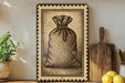 a framed illustration of a sack or bag, placed on a shelf next to a wooden cutting board and some lemons.