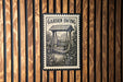 A garden swing is depicted on a wooden wall, with a black and white stamp-like design above it.