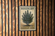 A vintage-style rosemary bush stamp is displayed on a wooden wall.