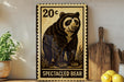 a large, detailed stamp-like artwork of a spectacled bear, with the text "SPECTACLEED BEAR" prominently displayed. The bear is depicted in a realistic style, with intricate details and shading that make it appear lifelike. The artwork is mounted on a wall, and there are some potted plants and kitchen utensils visible in the background.