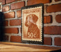A wooden table with a brick wall in the background, and a postage stamp featuring a dog's head is displayed on the wall.