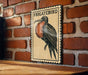 a wooden table with a framed illustration of a Frigatebird on it, mounted on a brick wall.