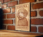A wooden sign with a stamp-like design, featuring a portrait of a curly-haired dog, mounted on a brick wall.