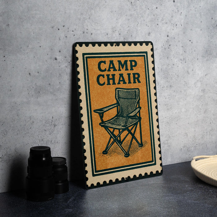 a metal sign with a camping chair illustration on it, placed on a table next to some black camera lenses.
