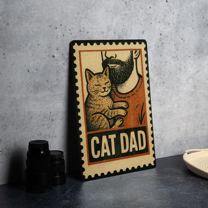 A metal sign with a cat and a man's face, along with the text "CAT DAD", is displayed on a table.