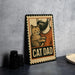 A metal sign with a cat and a man's face, along with the text "CAT DAD", is displayed on a table.
