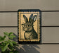 A sign featuring a cartoon image of a rabbit wearing glasses, mounted on a wall next to a plant.