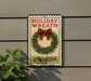 A metal sign with the text "HOLIDAY WREATH" and a wreath decoration is mounted on a wall.