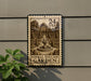 A metal sign with a stamp design, depicting a formal English garden, is mounted on a wall.