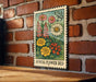 A metal sign with a floral design hangs on a brick wall, featuring a variety of colorful flowers and plants.