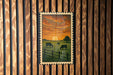 A framed painting depicting a pastoral scene with cows grazing in a grassy field, framed by a wooden fence.