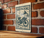 A wooden table with a bicycle on it, and a sign with a mountain and trees in the background, mounted on a brick wall.